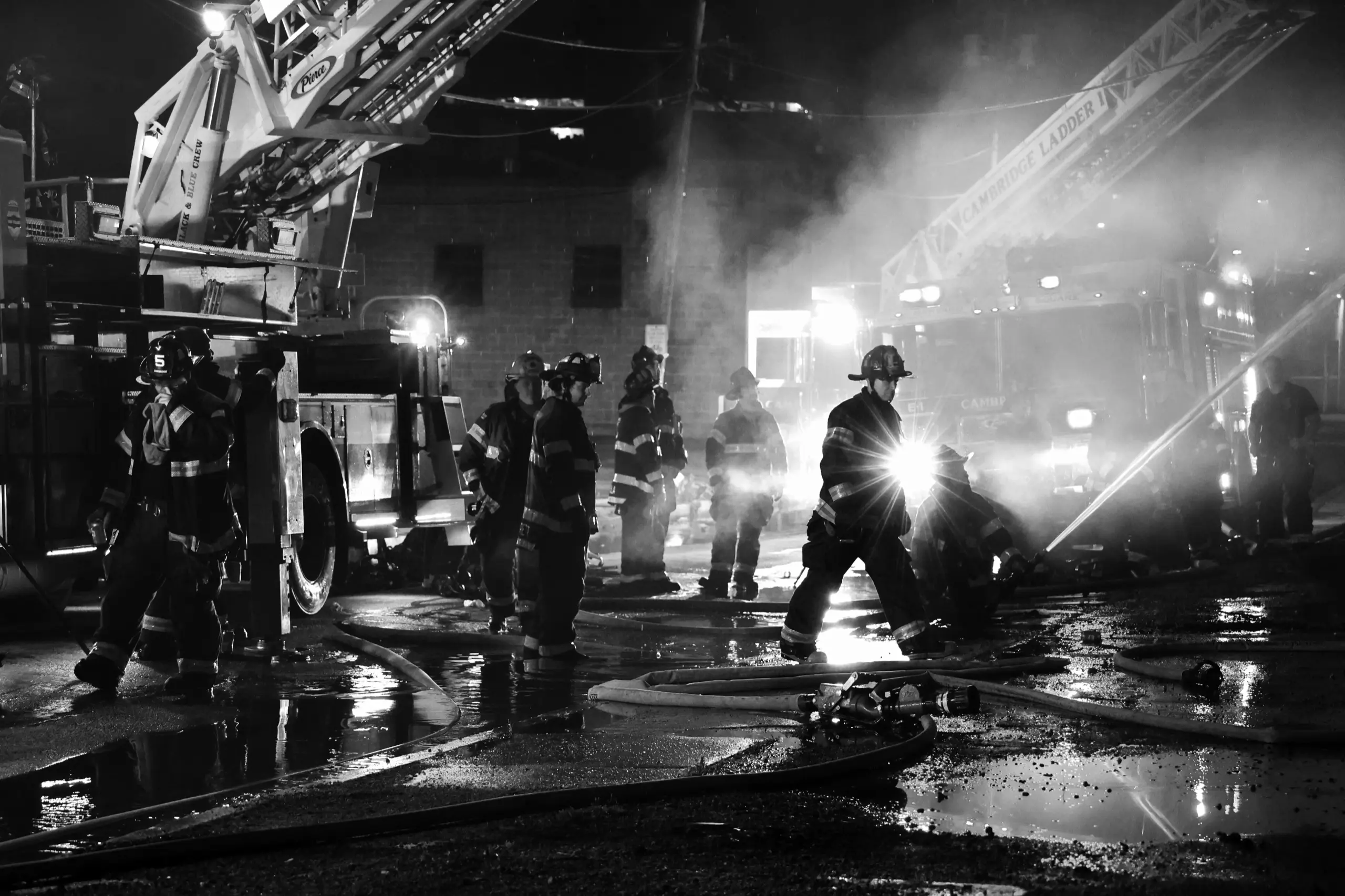 Firefighters working a nighttime fire scene with apparatus and hoselines