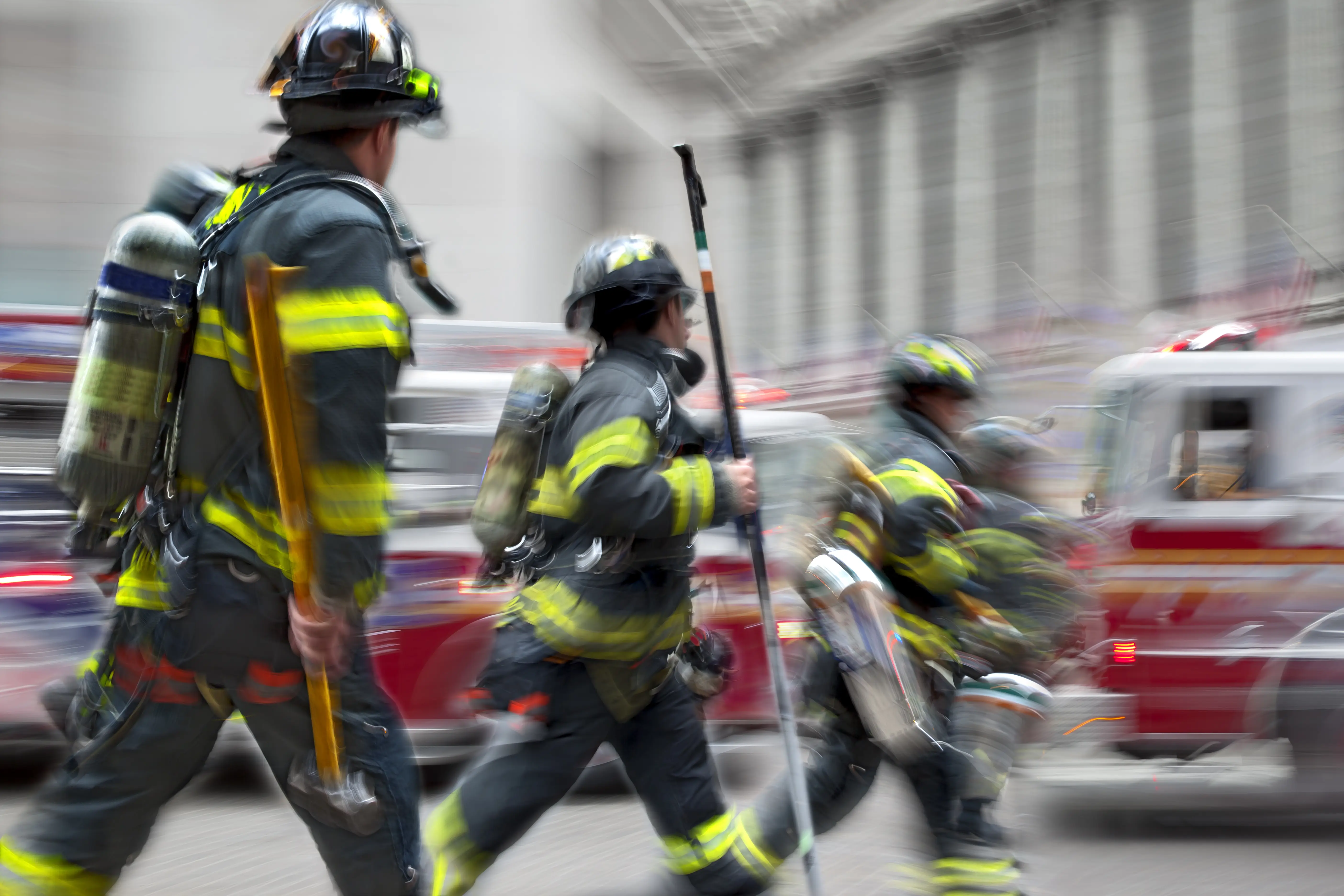 Firefighters walking with tools through a city street.
